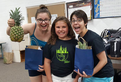 A student in Columbus, Wisconsin poses, wearing her Wizard of Oz t-shirt, with teachers Cathlyn Melvin and Cassandra Quinn, who hold the pineapples they received as teacher gifts.